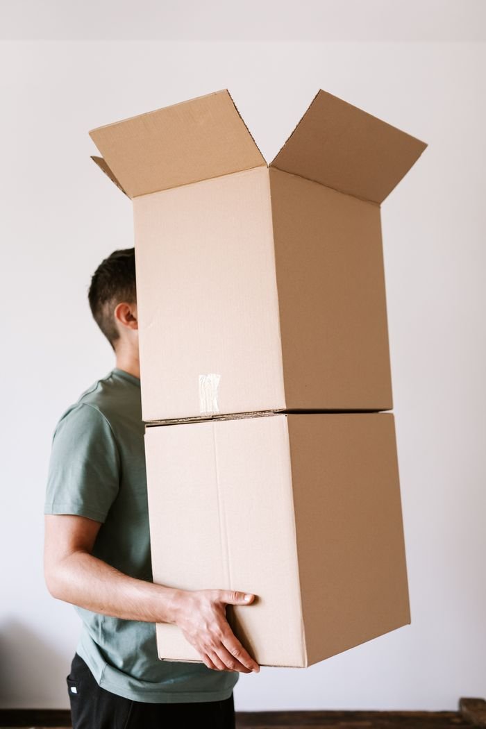 About Us Side view anonymous male in casual clothes carrying stack of opened carton boxes while moving into new apartment